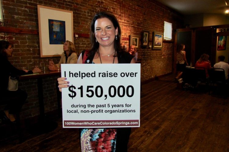 woman holding sign of amount raised for 100 women who care colorado springs